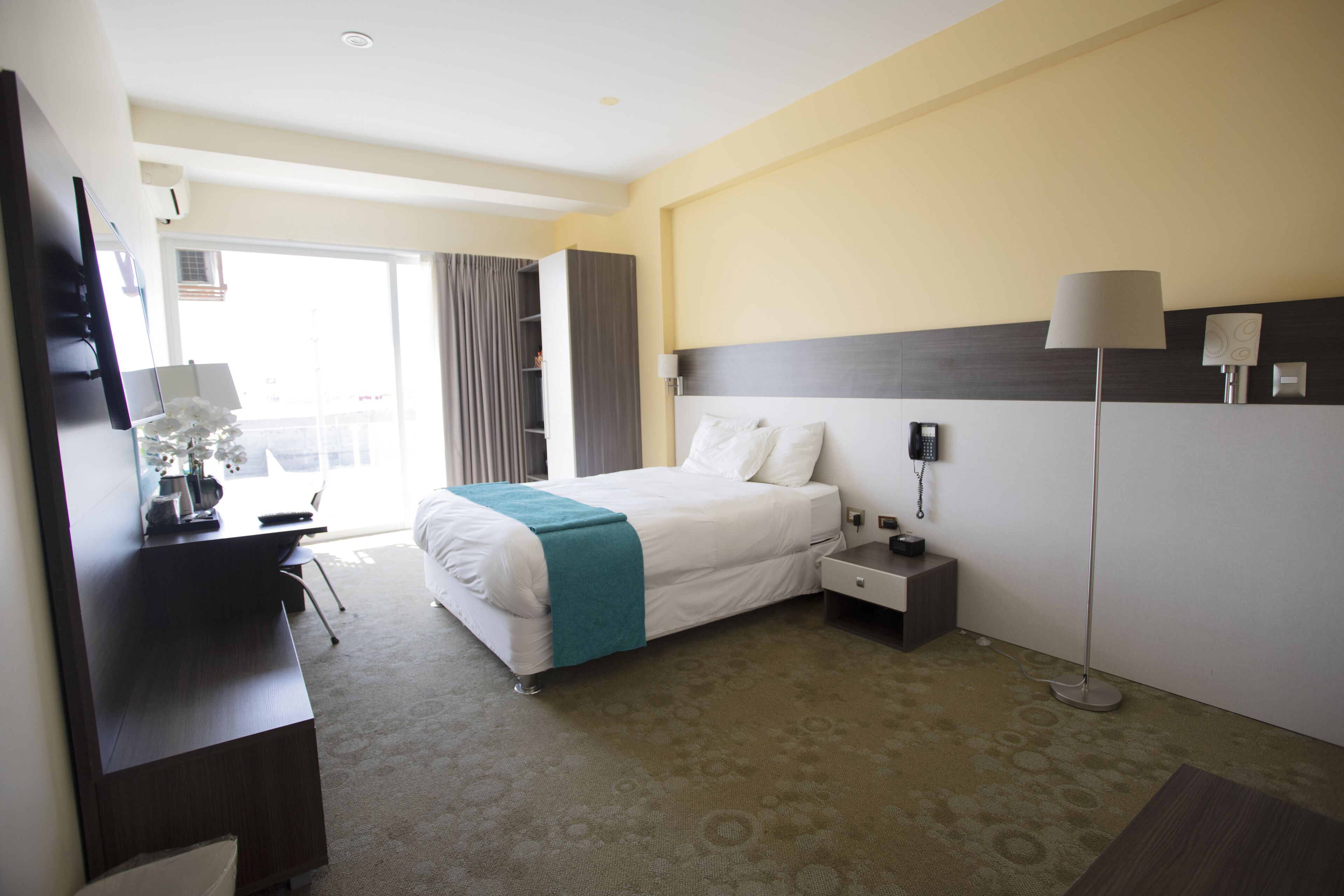 Une chambre d’hôtel avec un lit, un bureau et une chaise, une lampe et un téléphone sur la table de chevet.