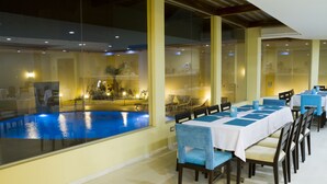 Un espace repas avec vue sur la piscine, des tables recouvertes de nappes bleues et des chaises dotées de coussins bleus et beige.