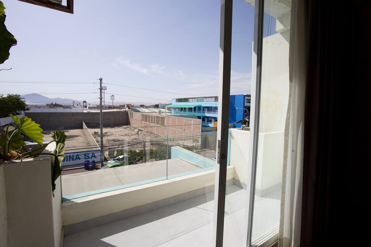 A view from a balcony with a clear sky, a construction site, and a blue building in the background.