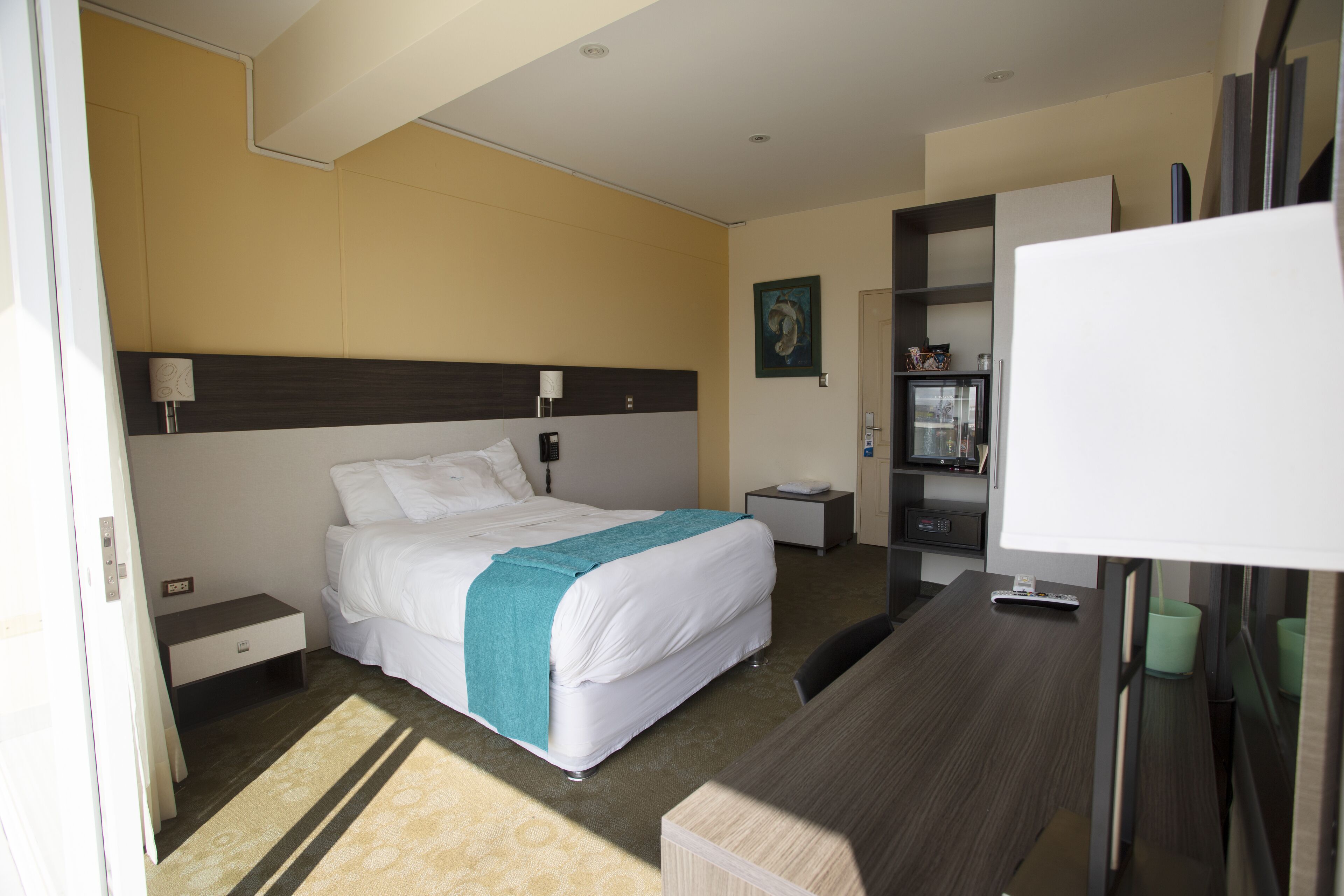 A hotel room with a bed, bedside table, lamp, and a desk with a chair.