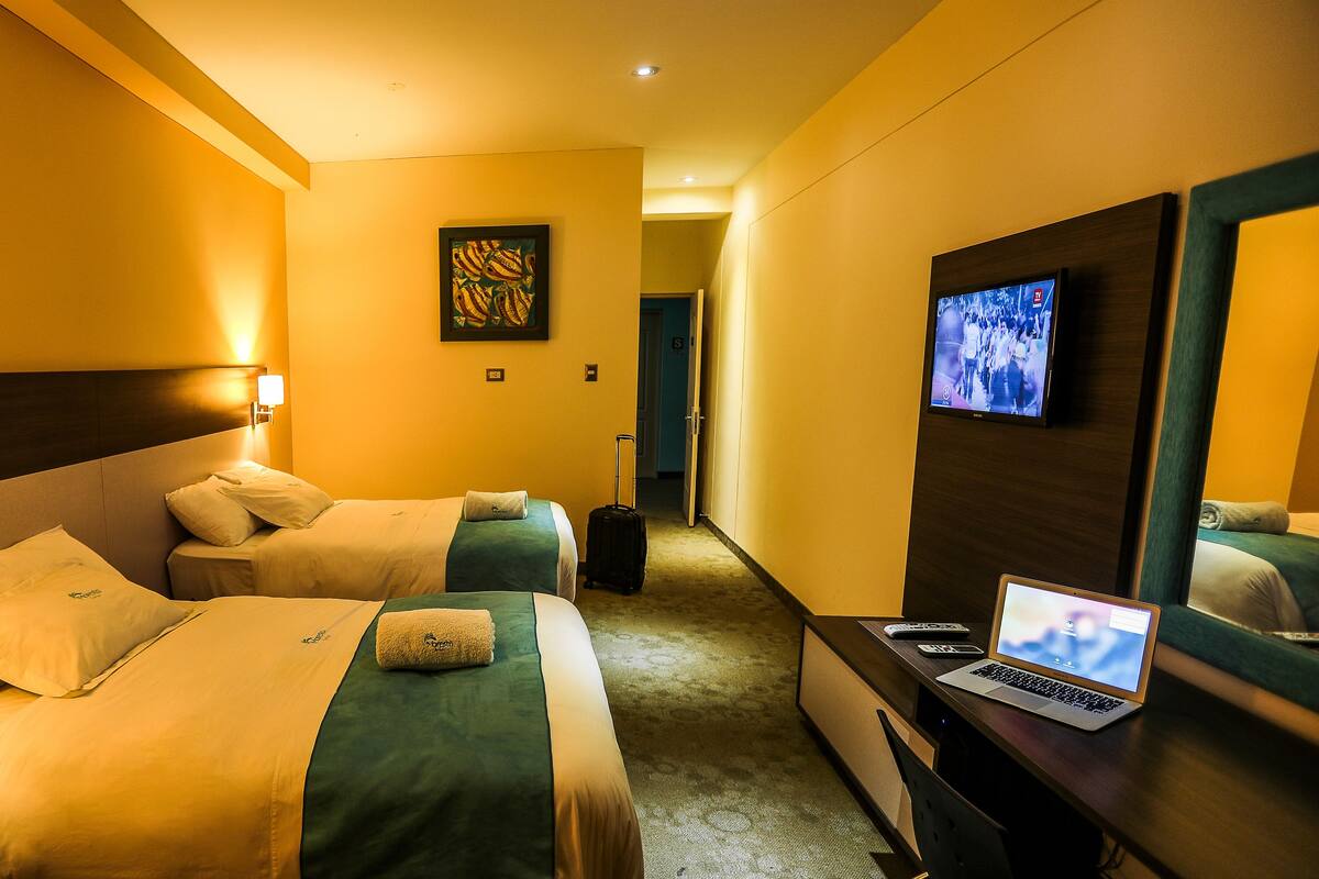 A hotel room with two beds, a desk with a laptop, a TV, and a painting on the wall.