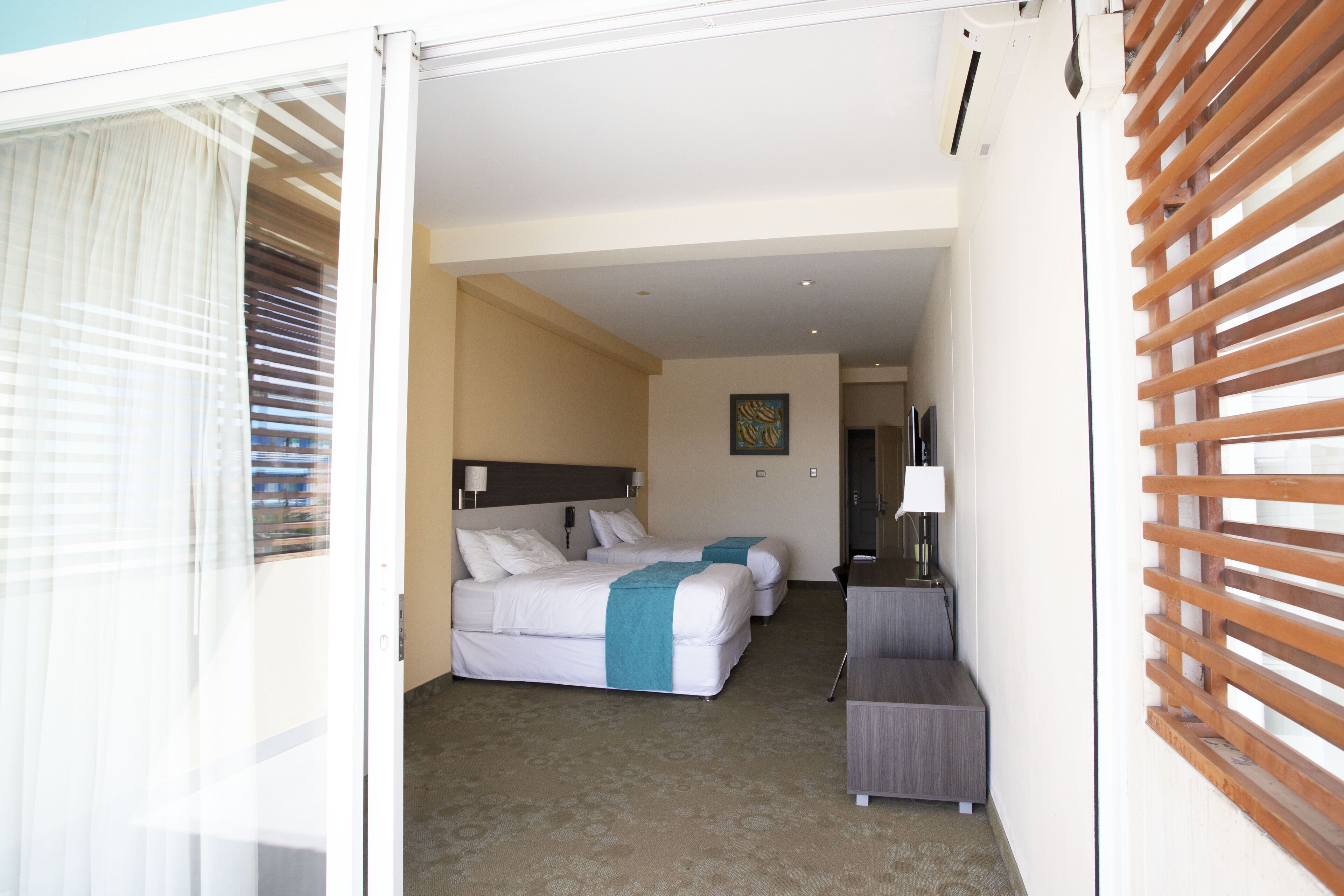 Habitación de hotel con dos camas, un escritorio y una ventana con persianas.
