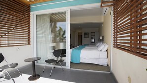 Un balcon avec une table et des chaises, un lit recouvert d’une courtepointe bleue et blanche, et une porte-fenêtre coulissante donnant sur une chambre.