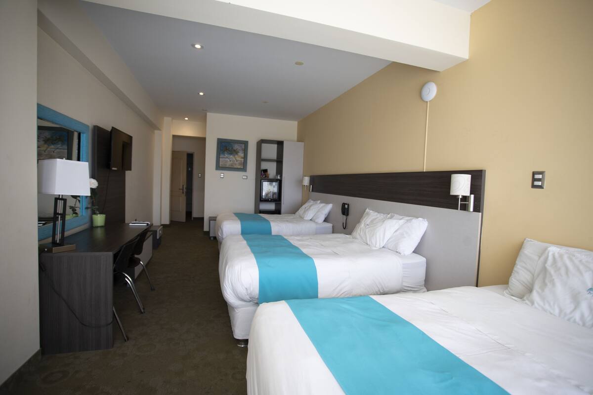 A hotel room with three beds, a desk, and a chair.