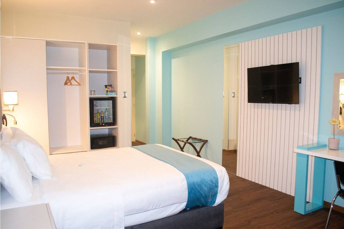 A hotel room with a bed, wardrobe, TV, desk, and a chair.
