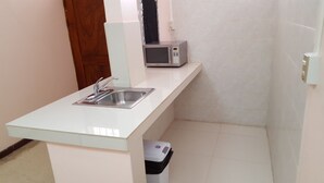A compact kitchen with a stainless steel sink, a microwave, and a trash bin. - Hotel Primavera (Liberia)
