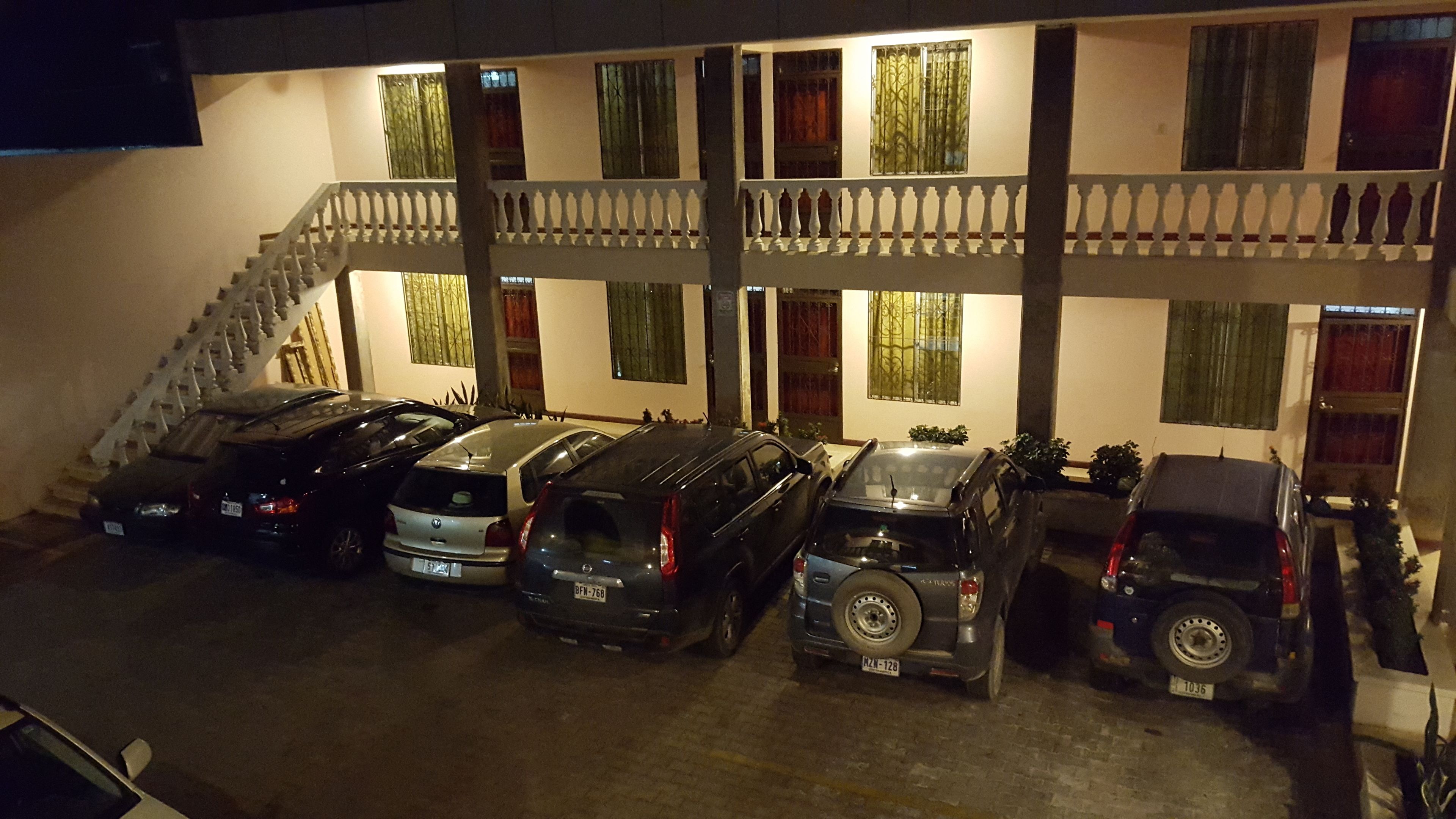Un estacionamiento con varios autos estacionados frente a un edificio con balcón.