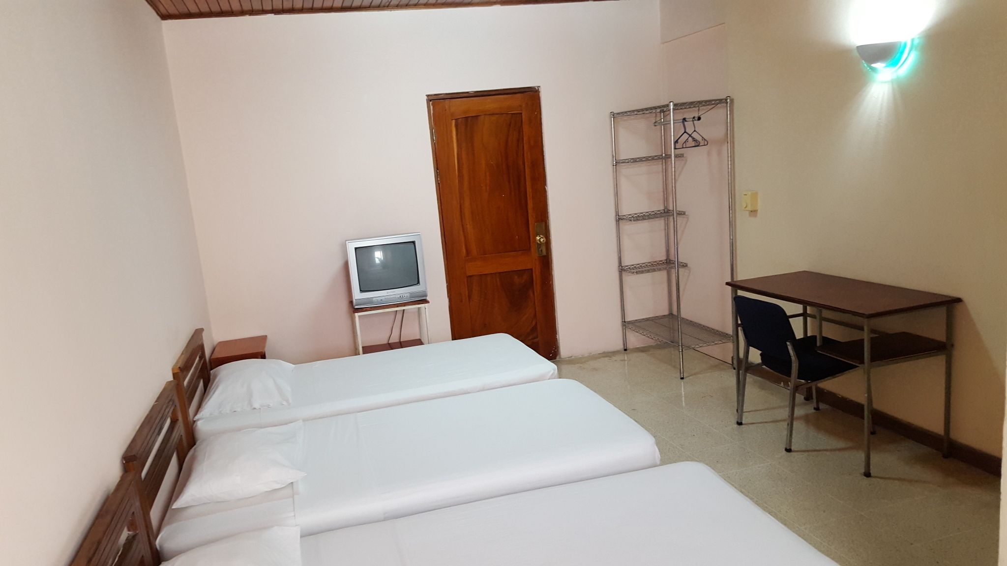 A small room with two beds, a wooden door, a TV on a small table, and a metal shelf unit.