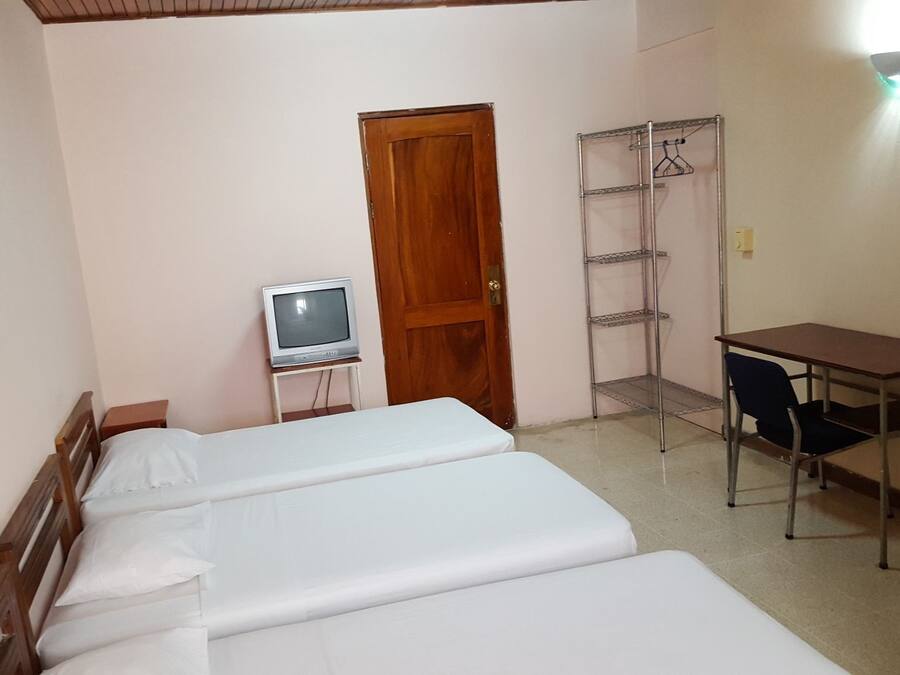 A small room with two beds, a wooden door, a TV on a small table, and a metal shelf unit.