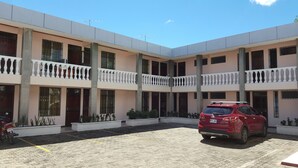 A multi-story building with balconies, a red car parked in front, and a paved courtyard. - Hotel Primavera (Liberia)