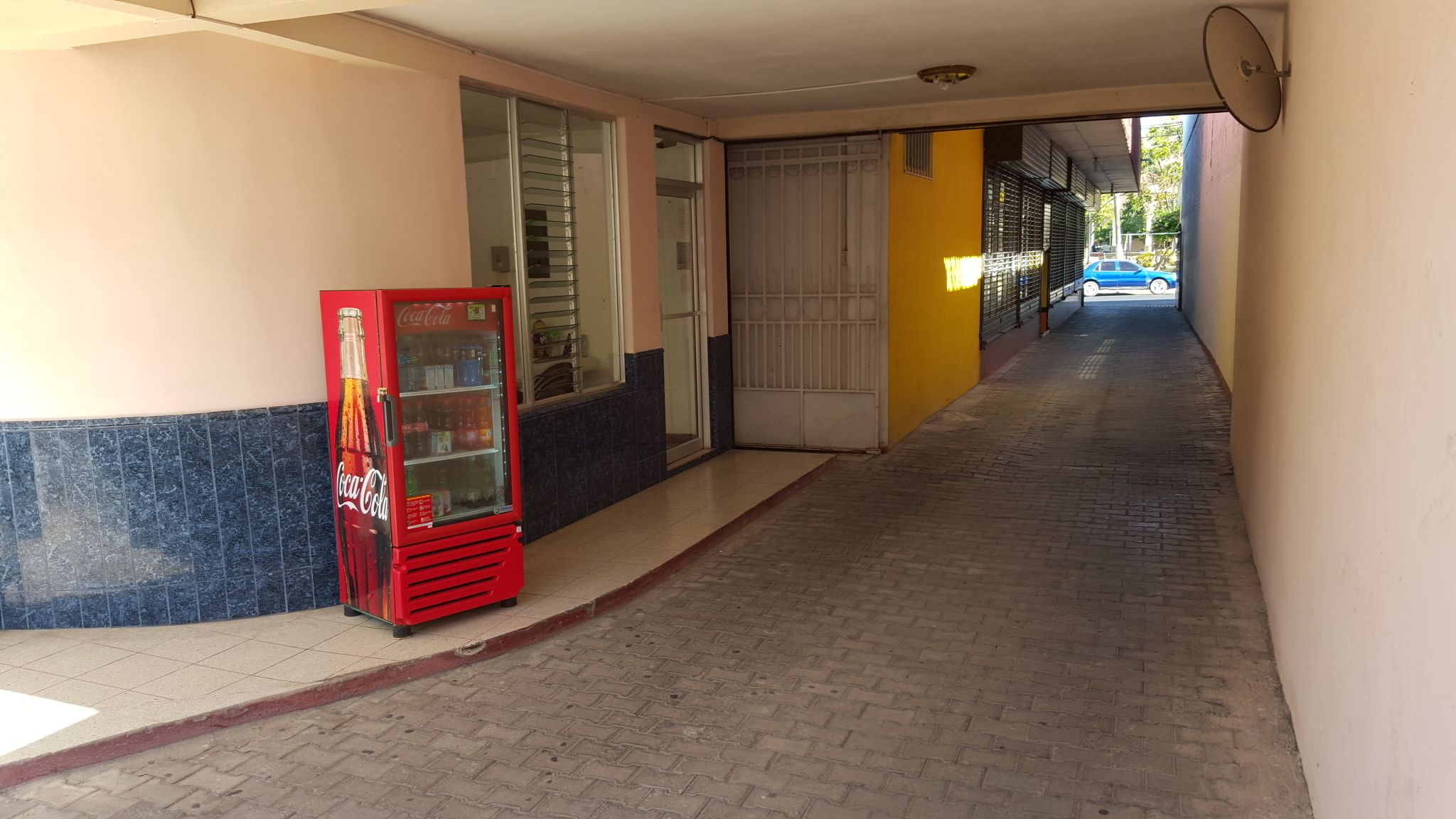 A corridor with a vending machine, a glass door, and a blue car parked outside.