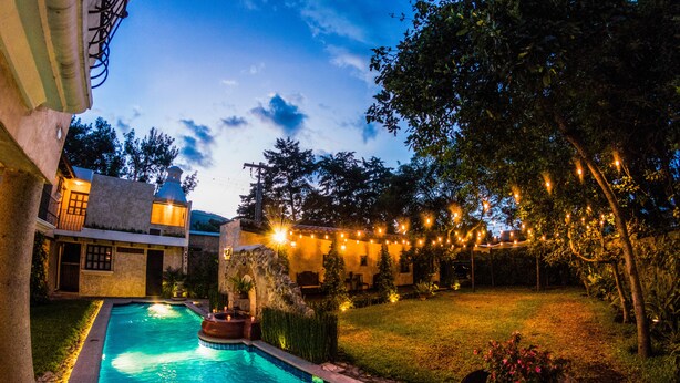 A swimming pool with a stone border, surrounded by a well-maintained lawn and trees. - Hotel Casa San Lázaro (Antigua Guatemala)