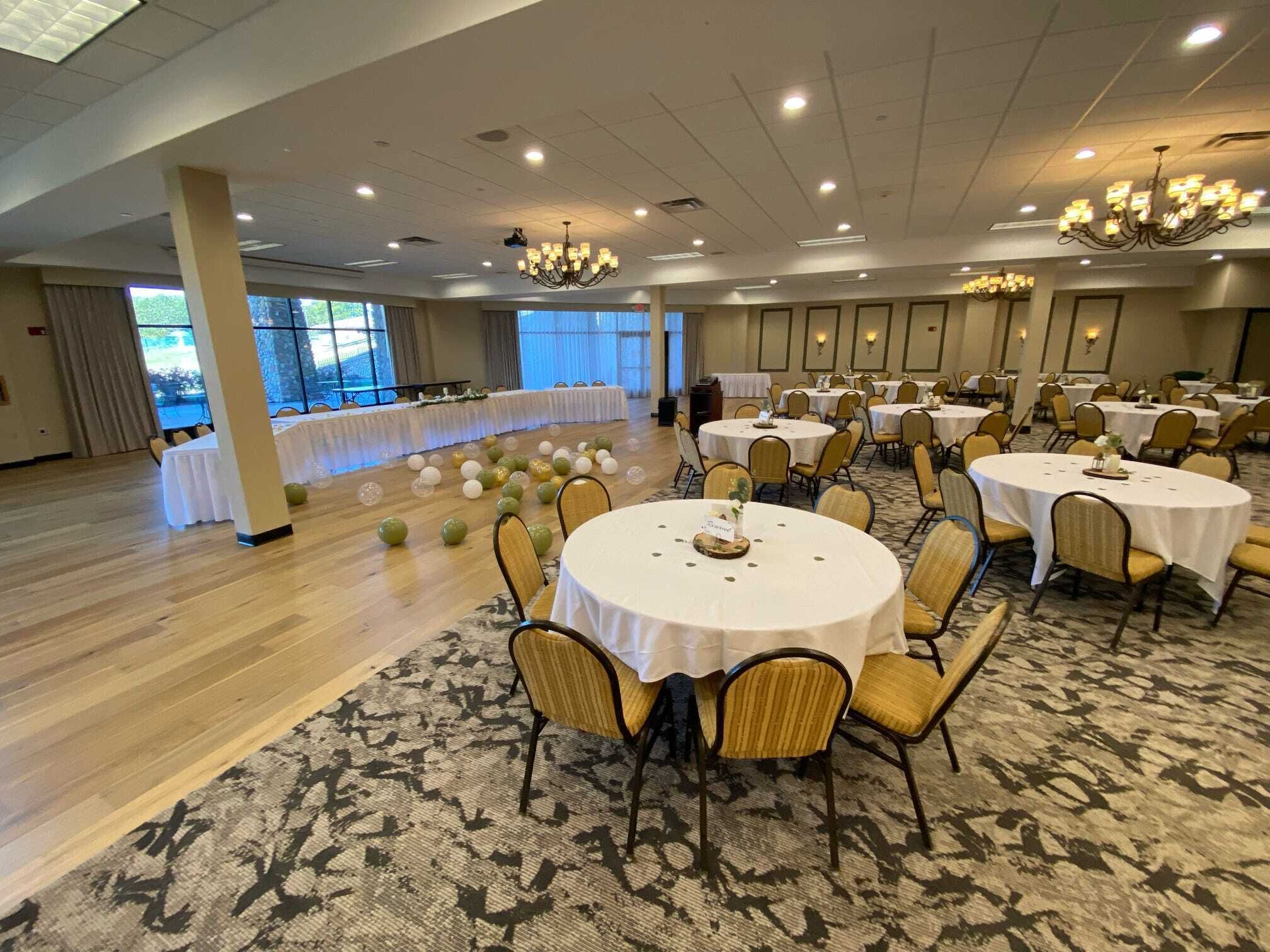 A banquet hall with round tables, chairs, and a long table with a white tablecloth.