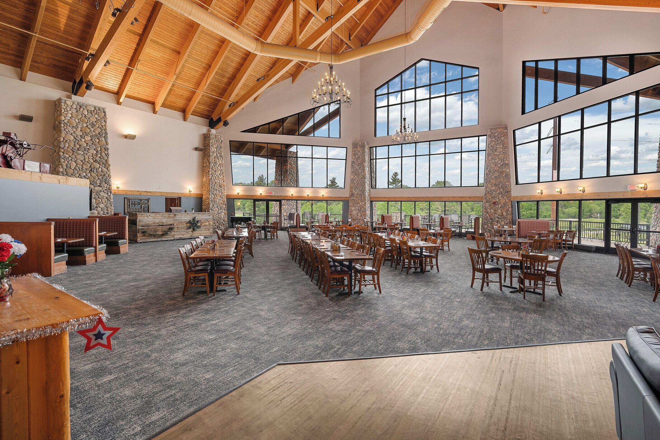A spacious indoor area with high ceilings, large windows, and wooden tables and chairs.