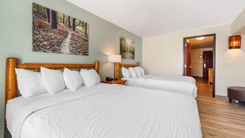 Habitación de hotel con dos camas, cabecero de madera, mesita de noche con lámpara y un cuadro de un sendero en el bosque en la pared.