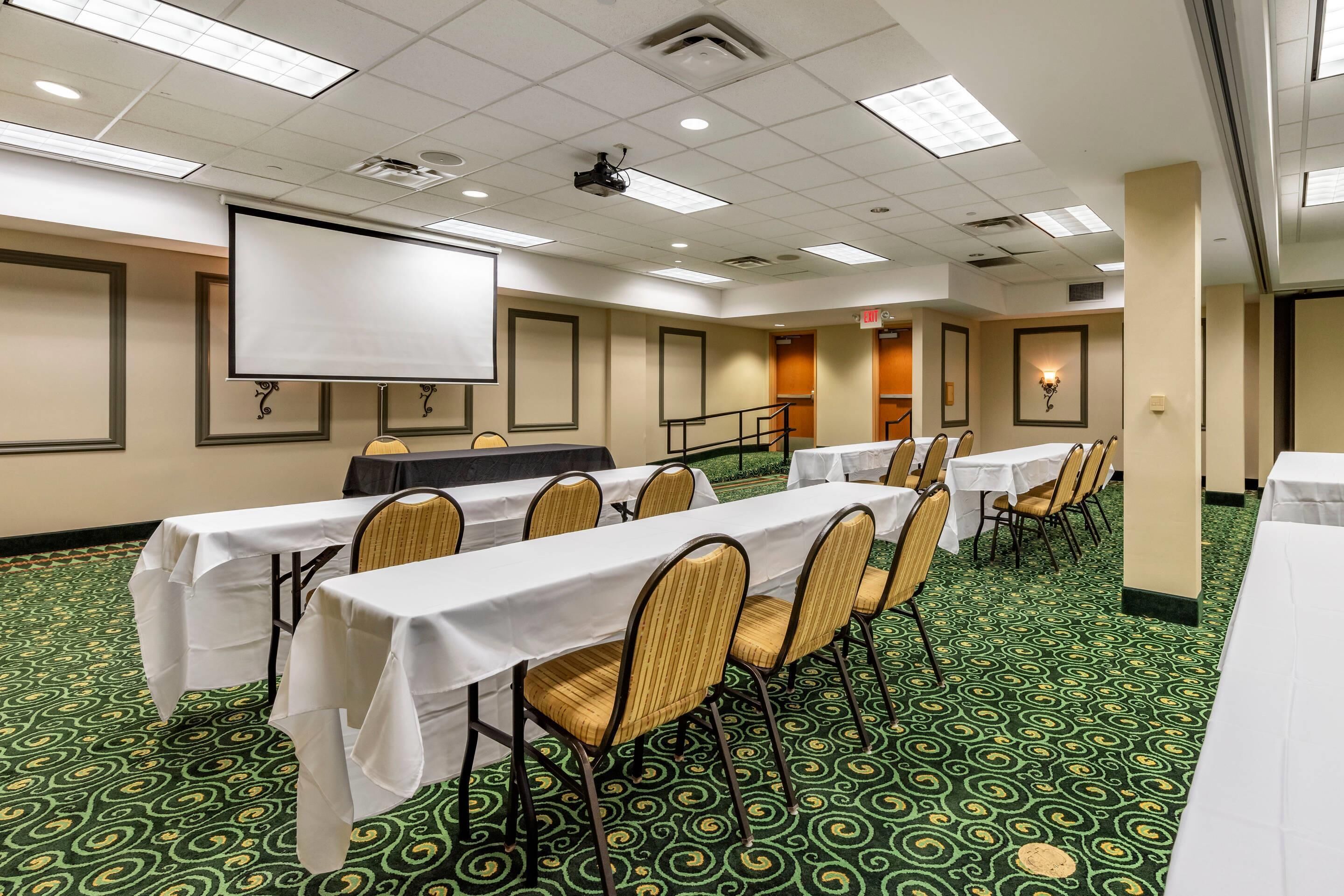 A conference room with tables and chairs, a projector screen, and a patterned carpet.
