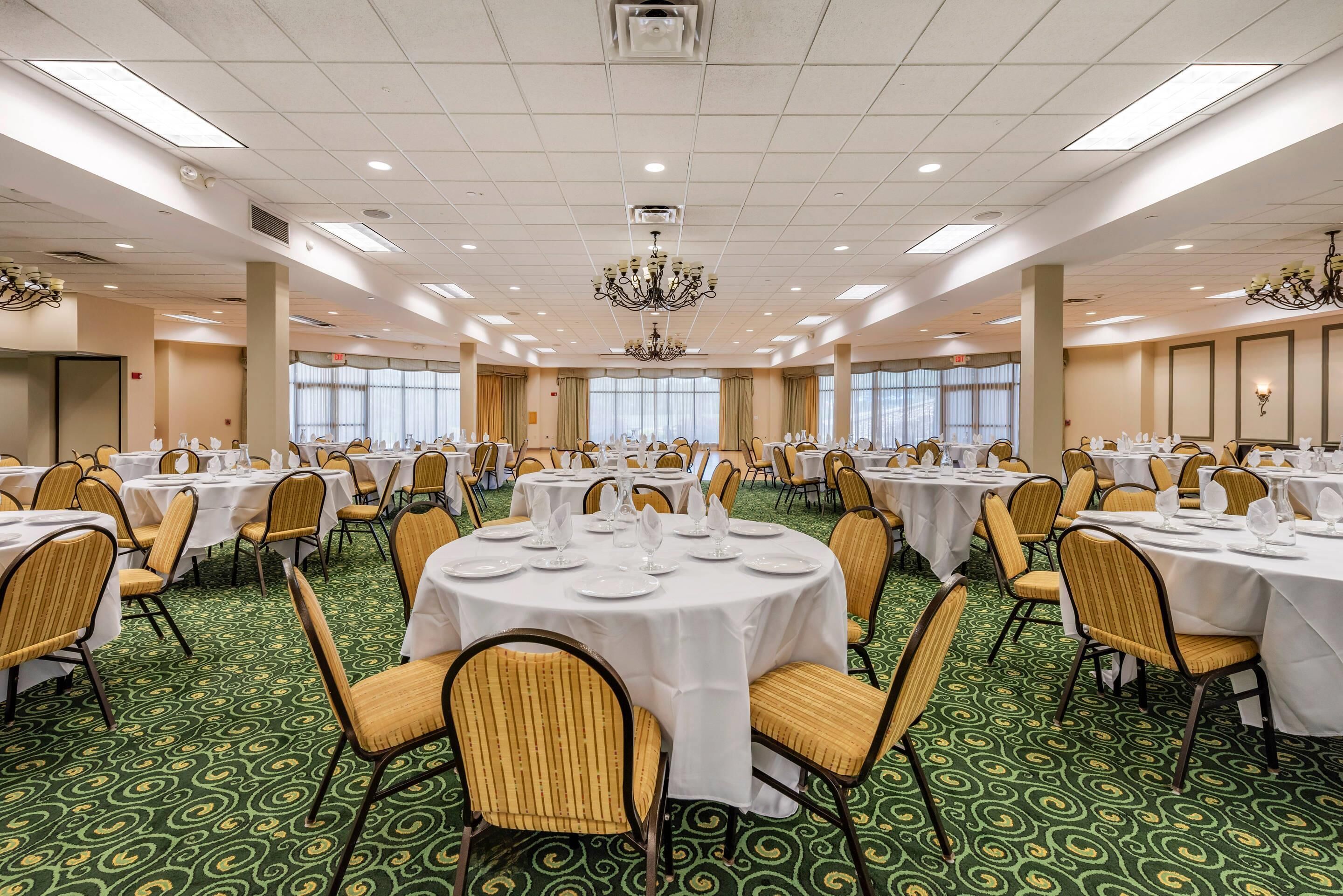 A banquet hall with round tables, chairs, and chandeliers.
