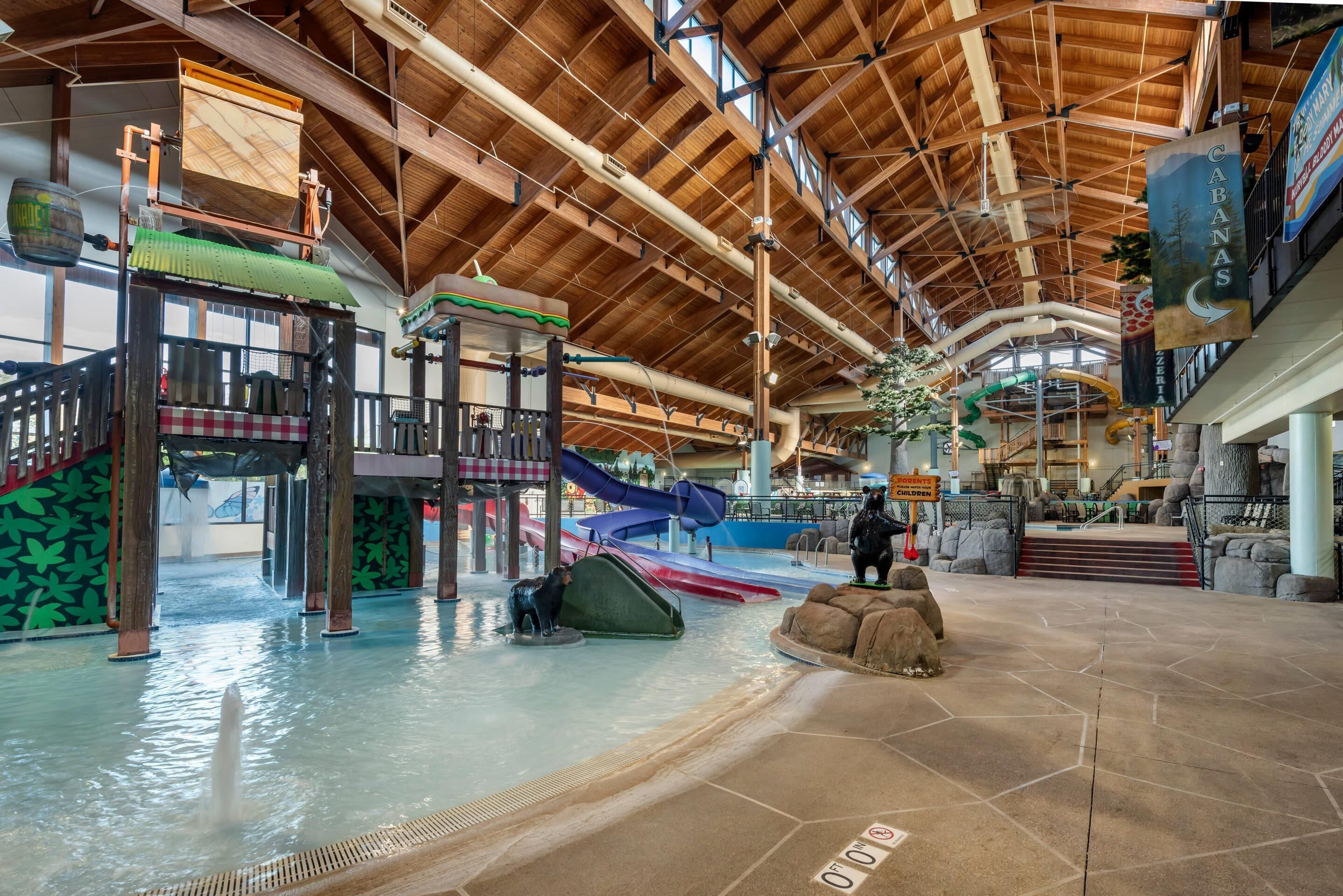 Een overdekt waterpark met glijbanen, een speelruimte en een houten plafond.