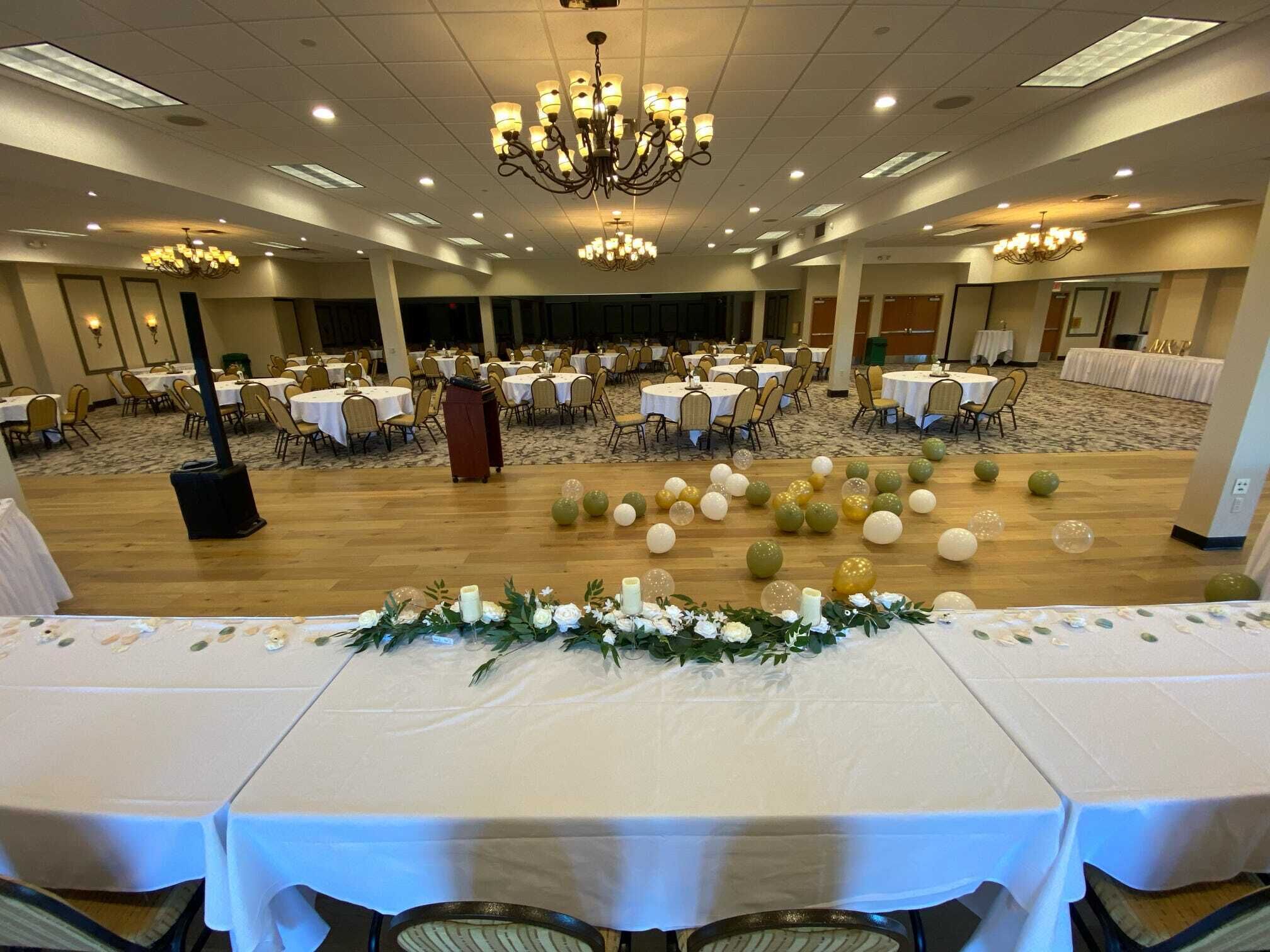 A banquet hall with multiple round tables, each covered with white tablecloths and decorated with floral centerpieces.