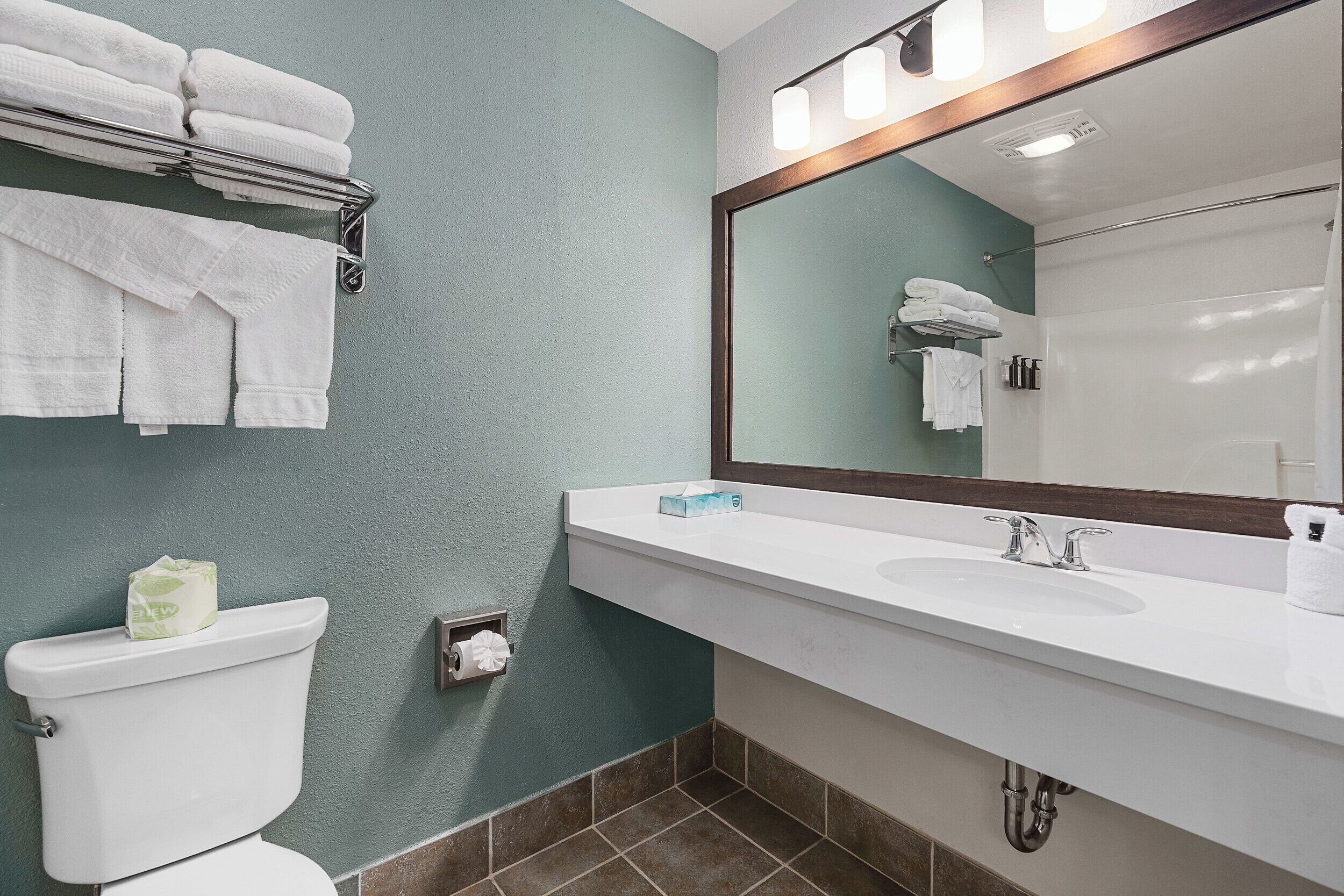 A bathroom with a white sink, a mirror, and a toilet. There are towels hanging on a rack above the toilet.