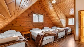 Acogedor dormitorio en ático con paredes de madera y techos inclinados, con tres camas dispuestas en fila.