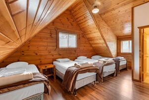 A cozy attic bedroom with wooden walls and sloped ceilings, featuring three beds arranged in a row.