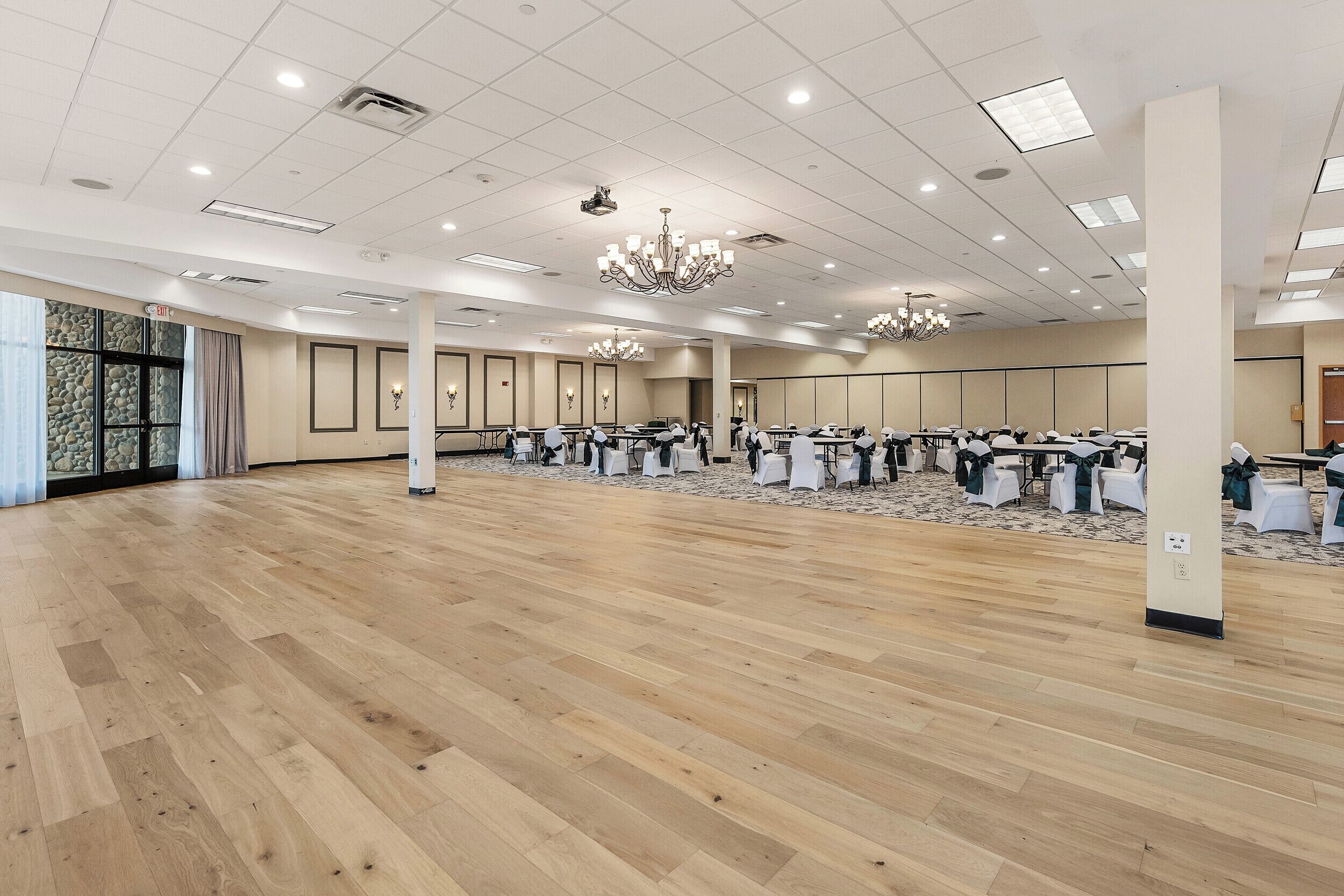 A large, well-lit conference room with wooden flooring, multiple tables, and chairs arranged for meetings.
