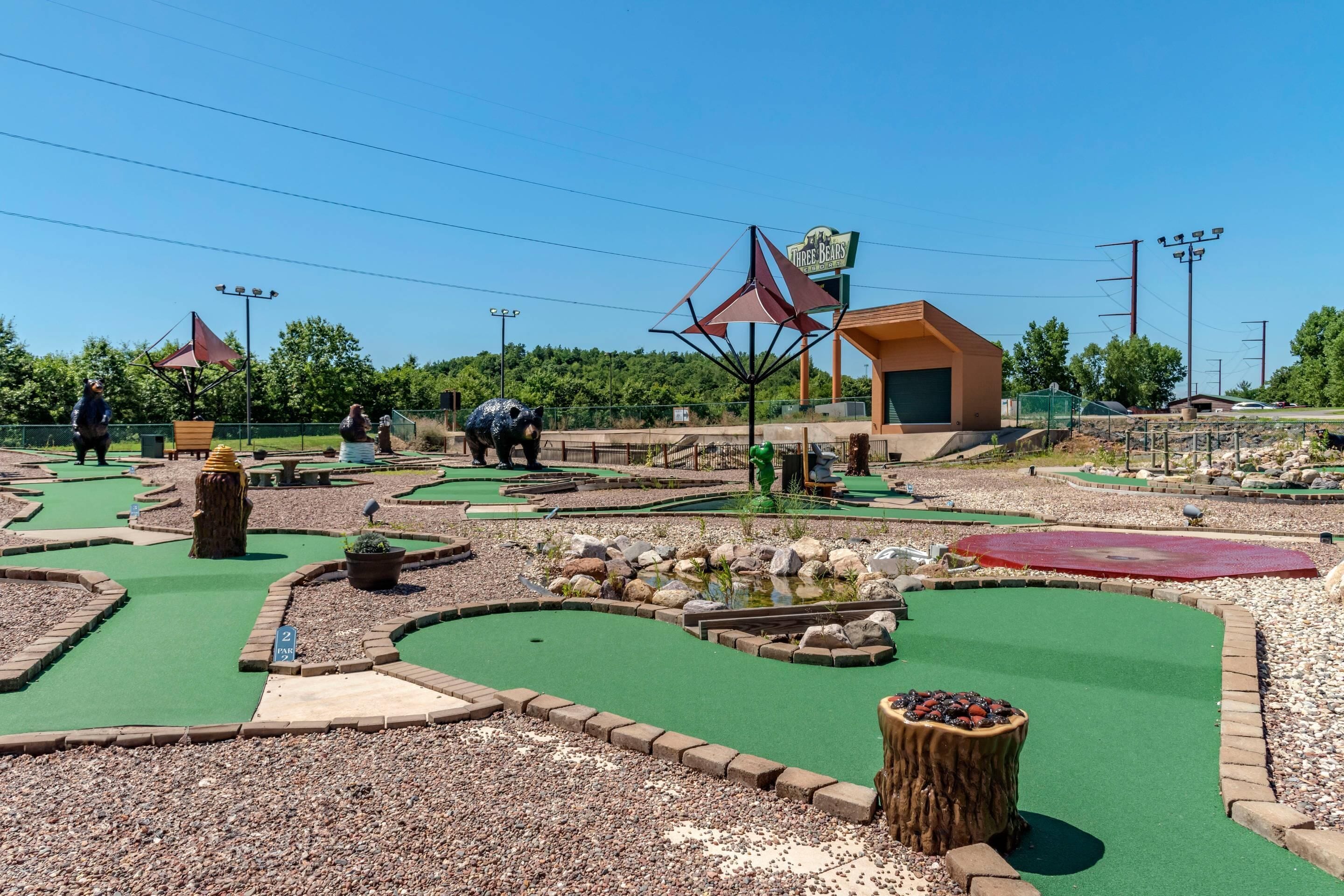 Un parcours de mini-golf avec différents obstacles et un petit bâtiment portant l’inscription « Les Trois Ours ».