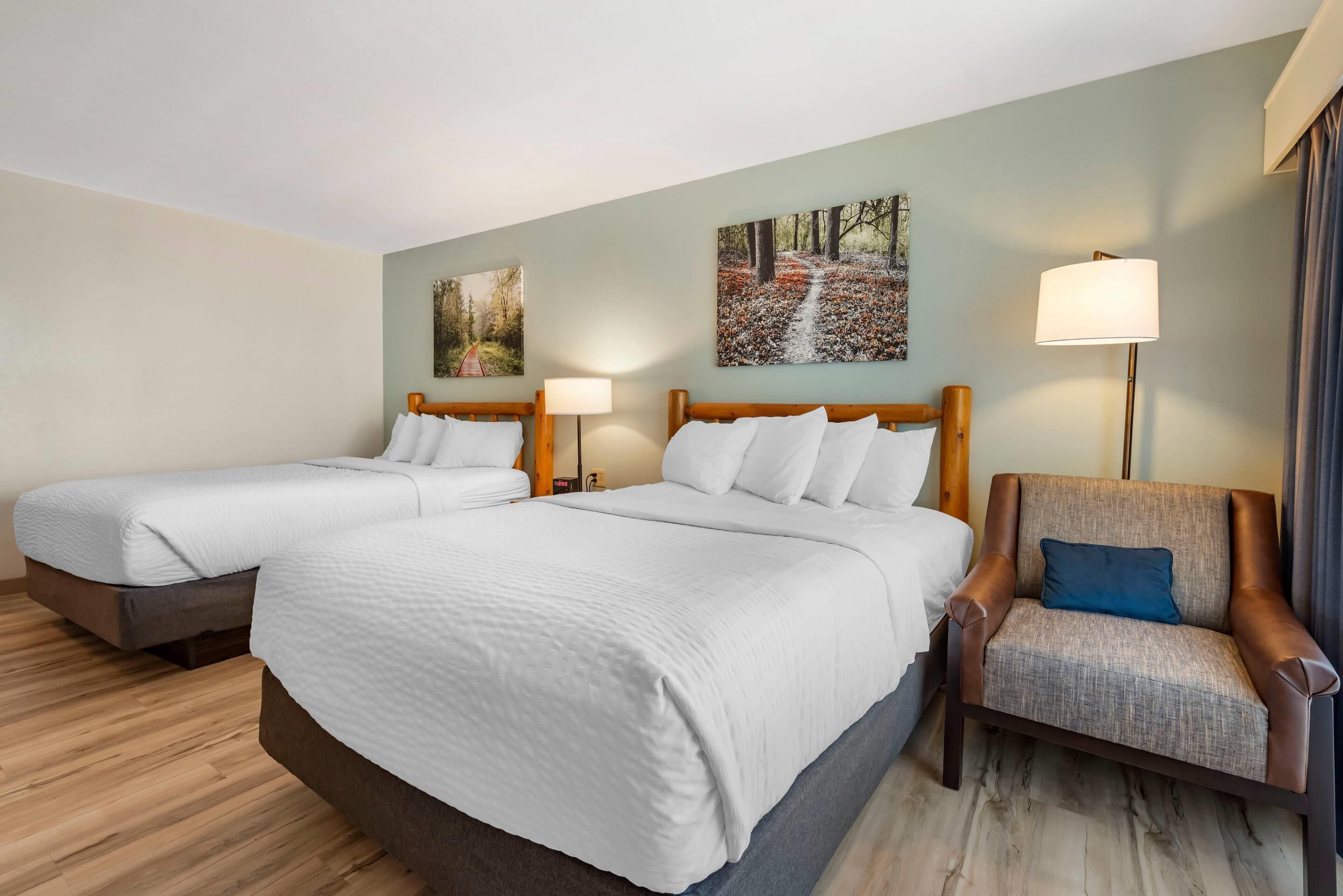 Habitación de hotel con dos camas, una silla y cuadros en la pared.