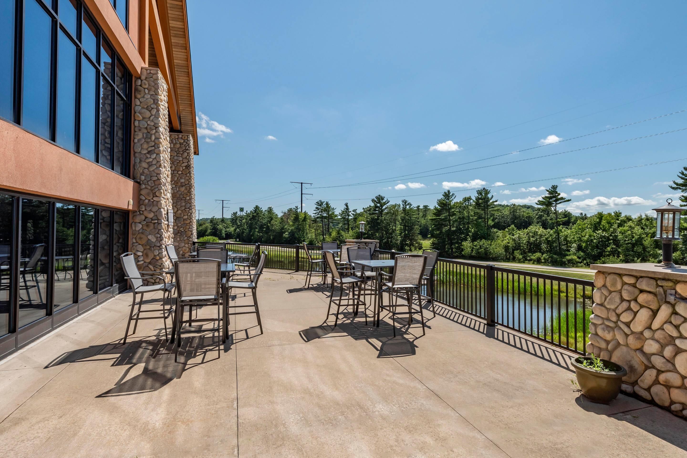 An outdoor patio with tables and chairs, a stone wall, and a view of a lake.