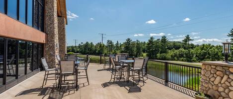 An outdoor patio with tables and chairs, a stone wall, and a view of a lake.