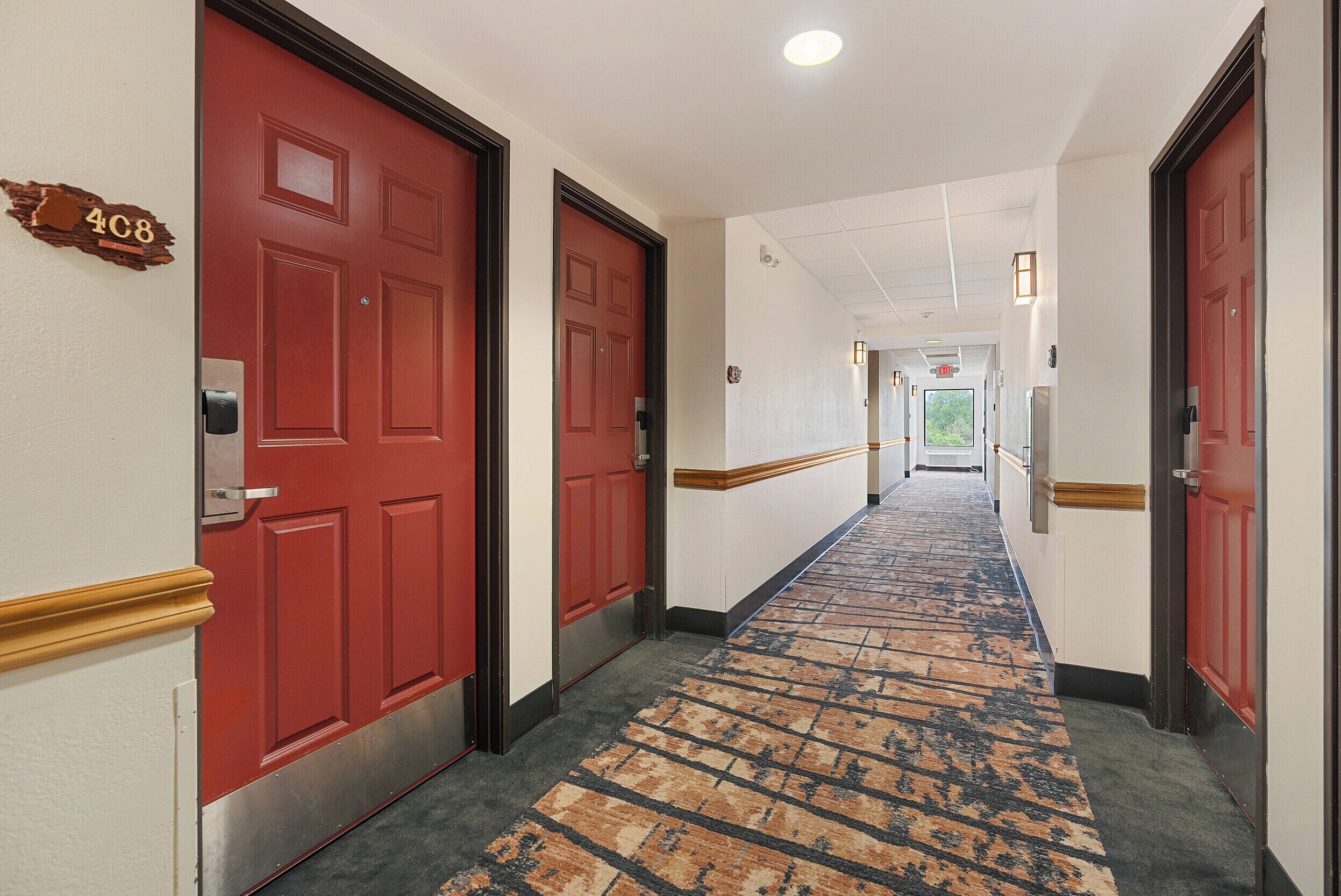 A hotel hallway with red doors, a patterned carpet, and a sign indicating room number 408.