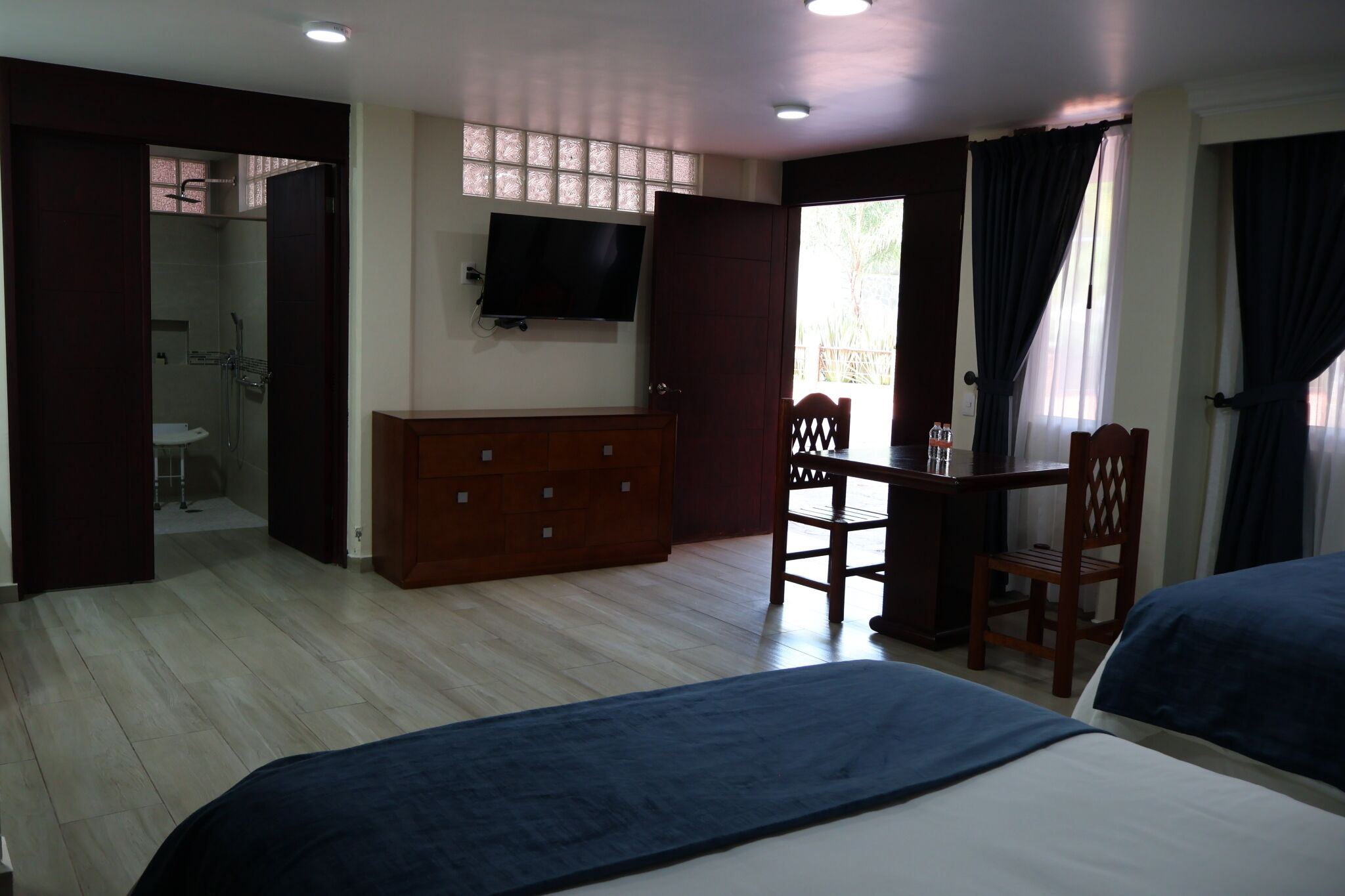 Habitación de hotel con cama, escritorio, silla, televisor y baño visible a través de una puerta abierta.