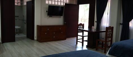 Habitación de hotel con cama, escritorio, silla, televisor y baño visible a través de una puerta abierta.