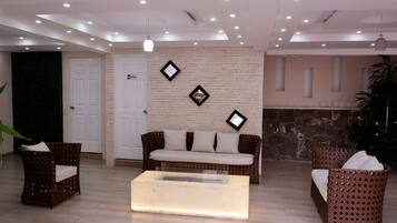 A reception area with a sofa, two wicker chairs, a coffee table, a brick wall, and a door.