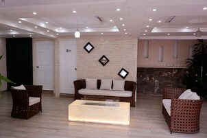 Zona de recepción con un sofá, dos sillones de mimbre, una mesa de centro, una pared de ladrillo y una puerta.