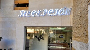 Una recepción de hotel con un gran letrero iluminado que dice "RECEPCIÓN" y un diseño de mariposa en la puerta de cristal.