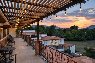Un hotel con un espacio exterior cubierto que cuenta con mesas y sillas, una pérgola con luces colgantes y vistas del paisaje circundante.