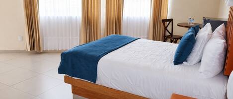 Una habitación de hotel con cama, mesita de noche, silla, ventilador y cortinas.