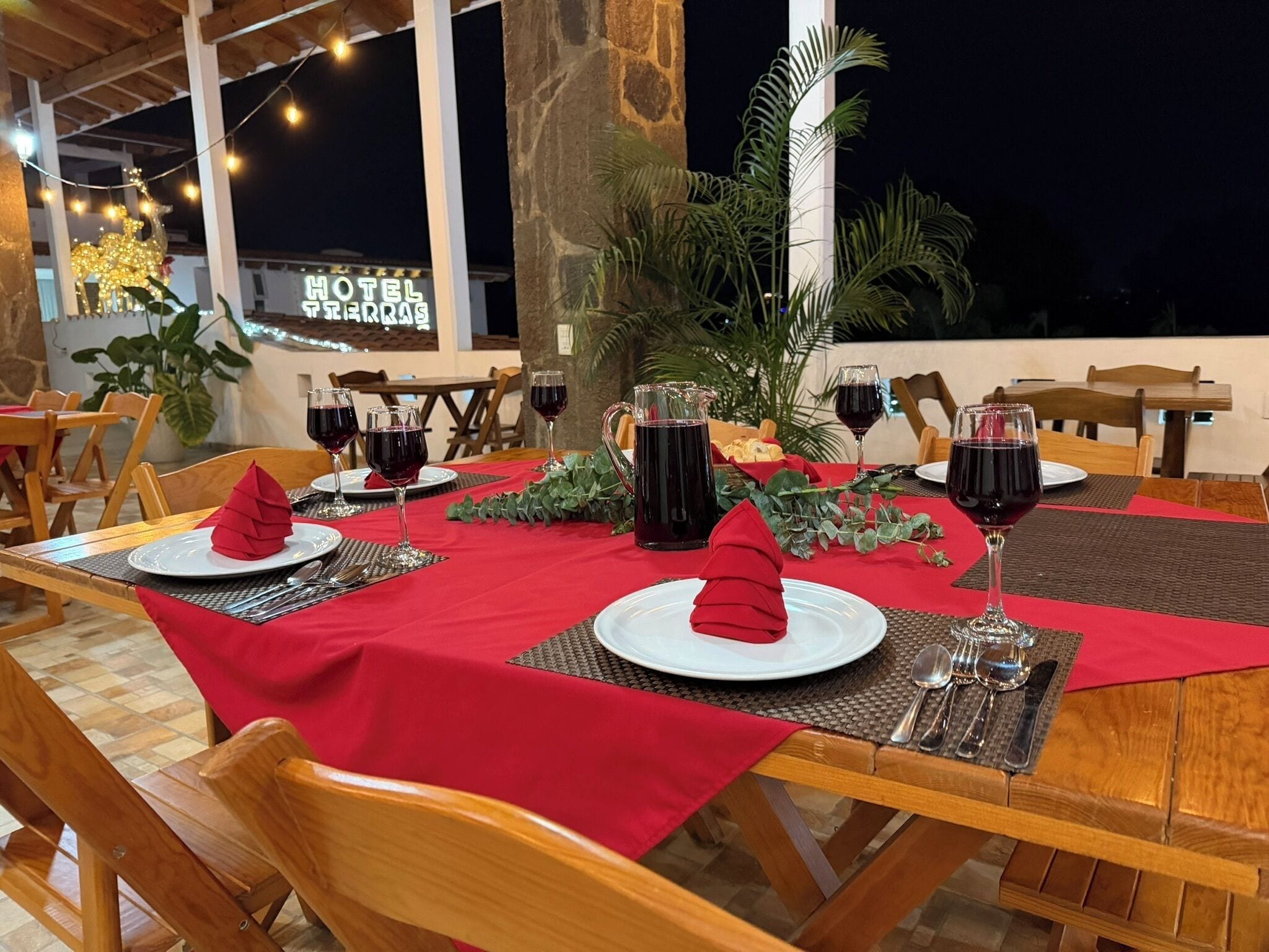 A restaurant setting with tables set for dining, featuring red tablecloths, wine glasses, and a view of the hotel in the background.