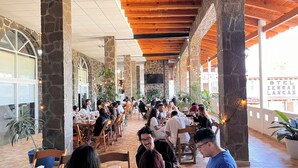 Un amplio comedor interior con pilares de piedra, vigas de madera y grandes ventanales.