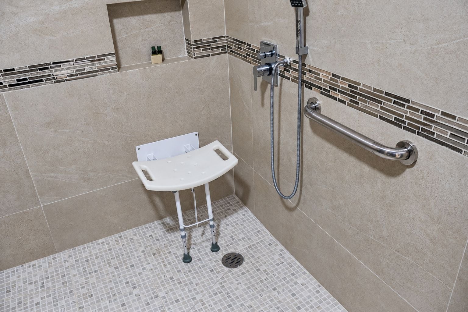 Une salle de bain avec une douche, une barre d'appui blanche et un sol carrelé.