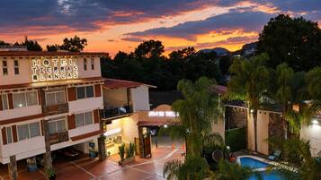 A hotel with a pool, surrounded by palm trees, at dusk.
