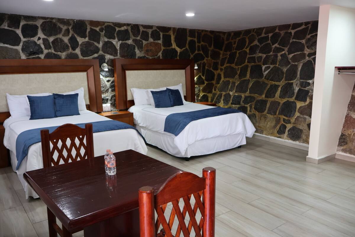 Habitación de hotel con dos camas, una mesa de madera y una pared de piedra.