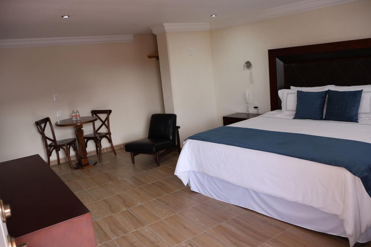 Una habitación de hotel con una cama grande, un escritorio con sillas y una mesita con dos botellas.