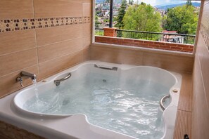 Uma banheira com água corrente, vista da cidade pela janela e parede revestida com detalhes decorativos.