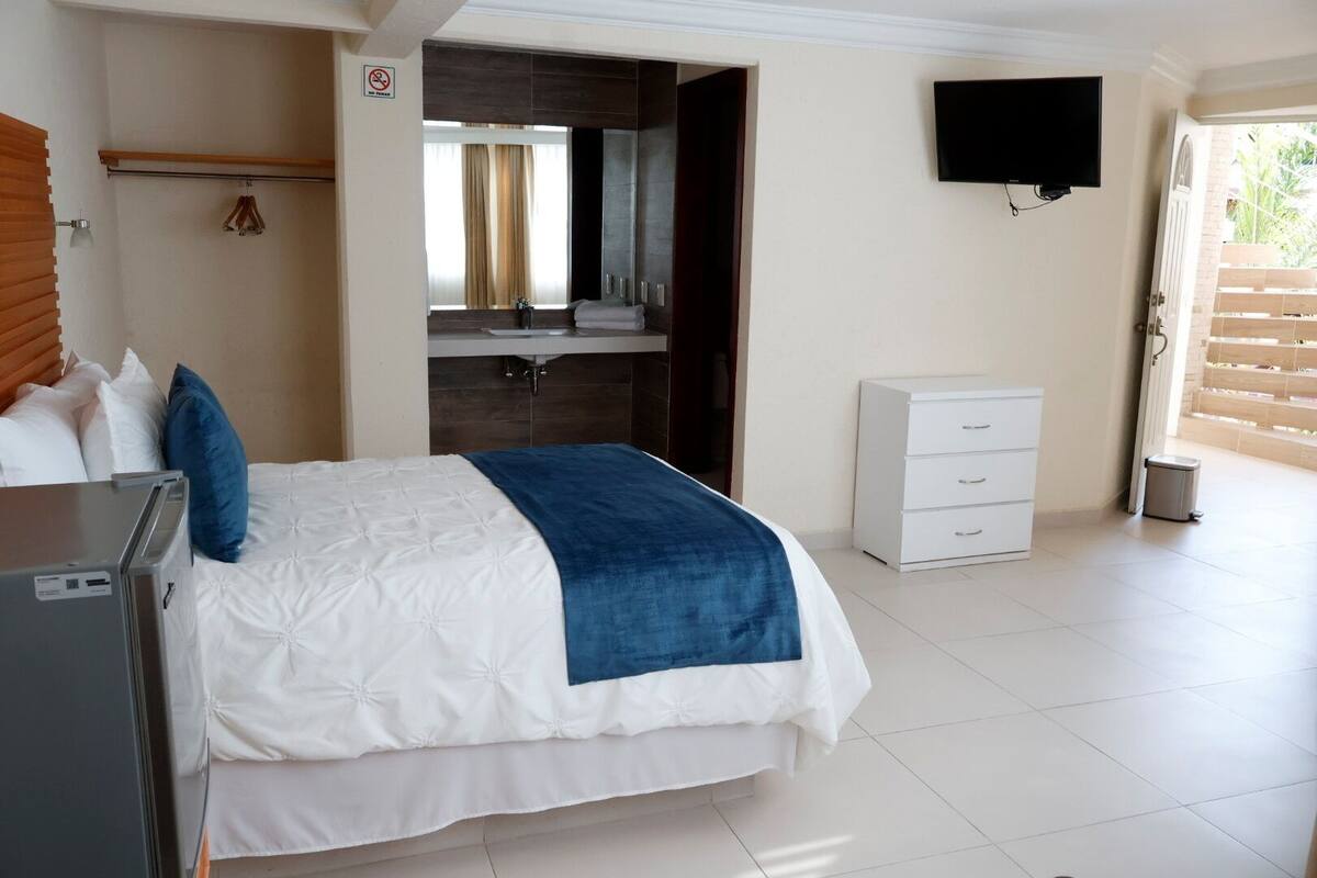 Habitación de hotel con cama, escritorio, televisión, baño y vistas al exterior.