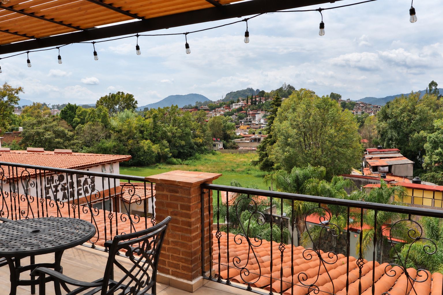 A balcony with a view of a town, a table, and chairs.