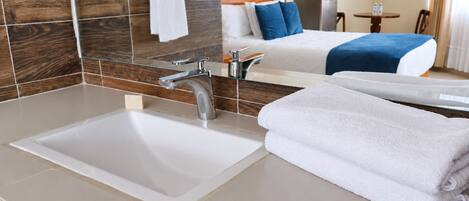 Un baño de hotel con un lavamanos grande, un espejo y una cama con ropa de cama azul.