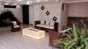 Una sala de estar moderna con mobiliario de mimbre, una mesa de centro de vidrio y una pared de ladrillo.